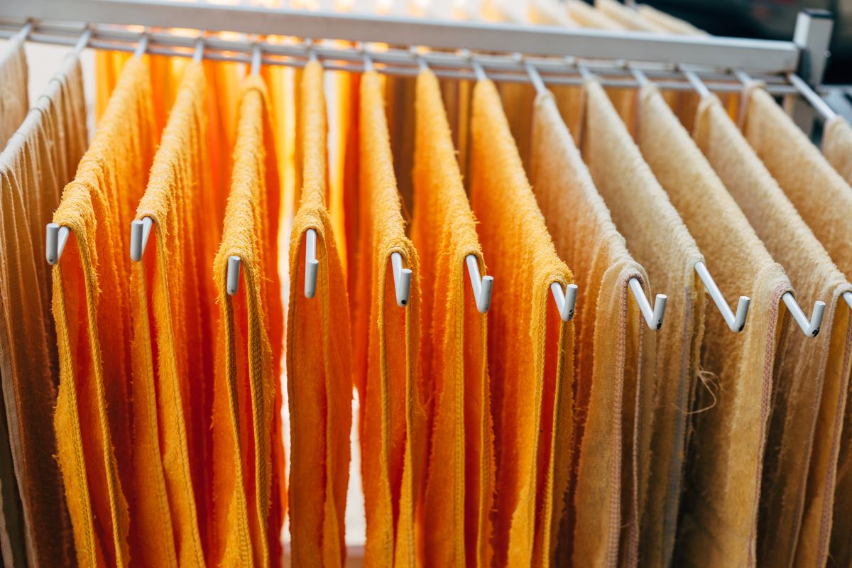 A clothes drying rack with spaced-out shirts and towels near a bright apartment window with the radiator turned off beside it