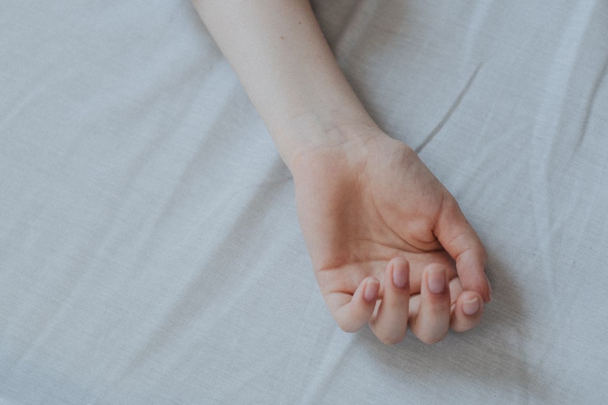 A hand pressing into a thick white memory foam mattress topper on a bare mattress, showing the slow recovery imprint