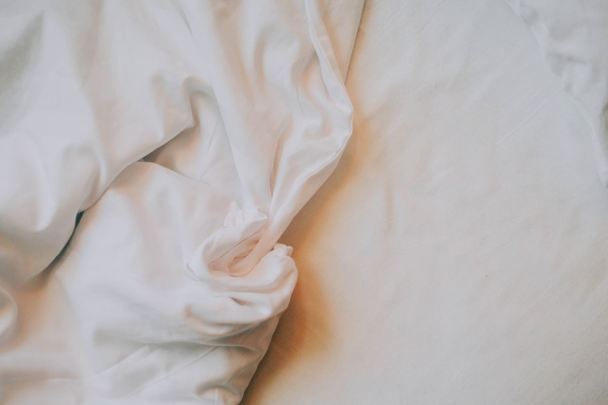 Crisp white percale bed sheets with a soft natural crinkle, lit by gentle morning light across the bed