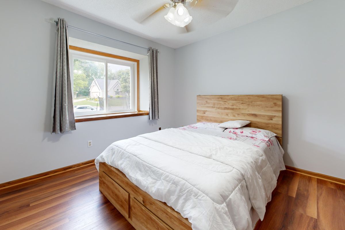 A minimalist bedroom with a low wooden platform bed frame, white duvet, and a wide window letting in natural daylight