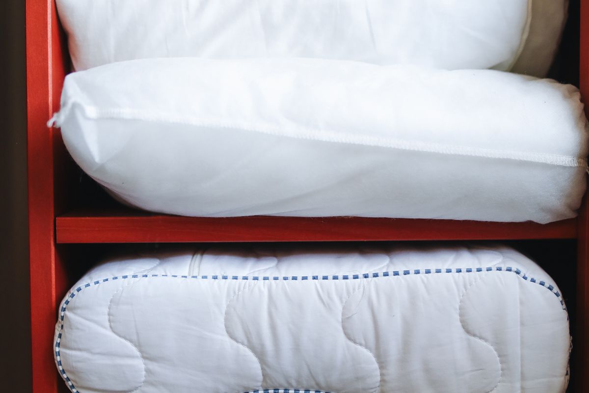 An organized linen closet with folded white sheet sets standing upright in file-fold style, rolled towels in labeled bins, and clear shelf spacing