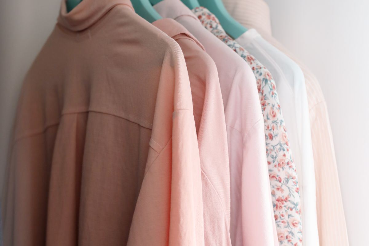 A small reach-in closet with neatly spaced identical hangers, folded sweaters on shelves, and labeled bins on the top shelf in natural light