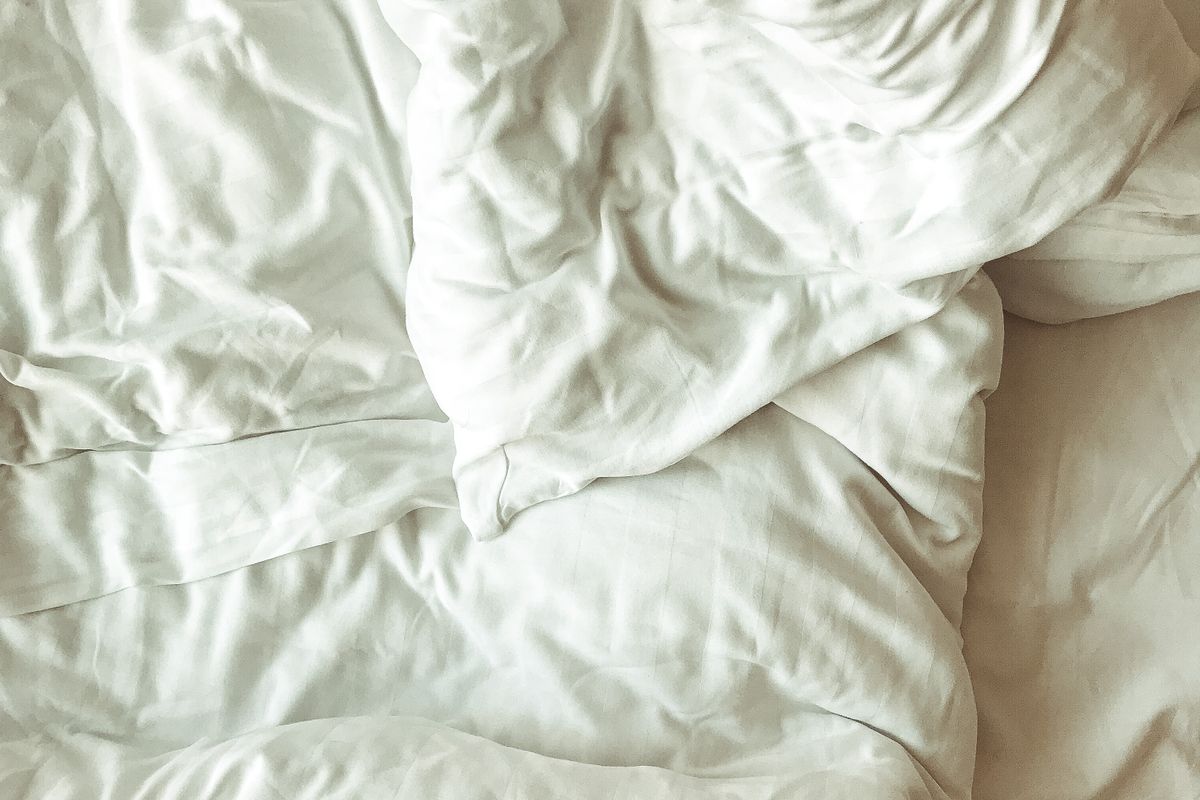 An extreme close-up of fine white cotton bed sheet fabric showing its woven texture under soft window light